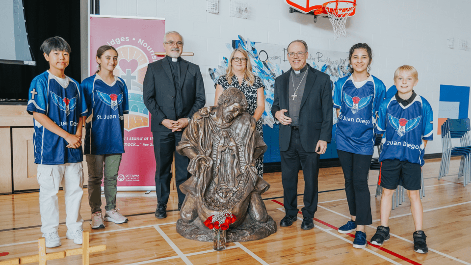 OCSB students teacher and priests beside a St Juan Diego statue
