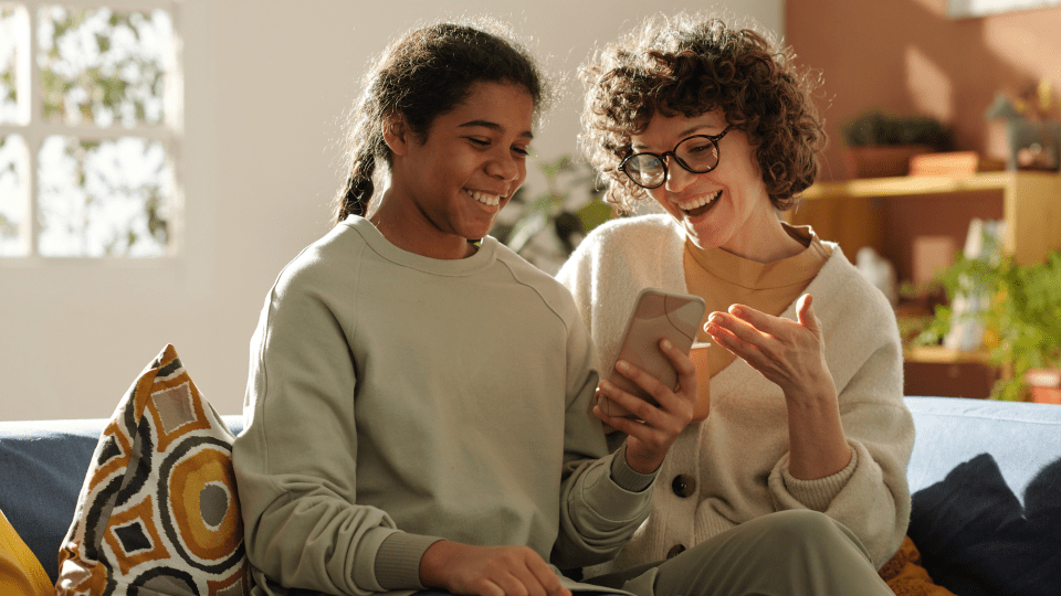 two girls smile while looking at a phone screen