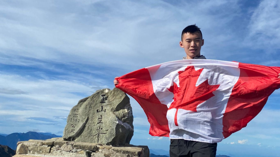 Ji-Hong Wu holding the Canada flag from the top of the mountain